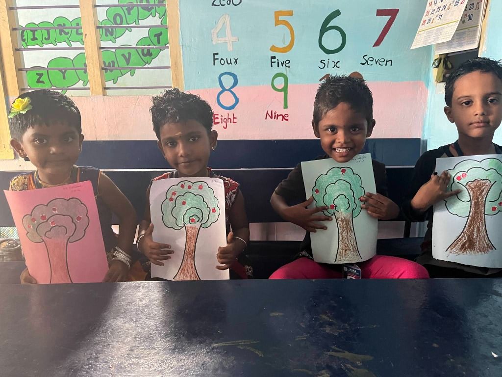 Four small children proudly holding up their apple-tree drawings in front of a painted number wall