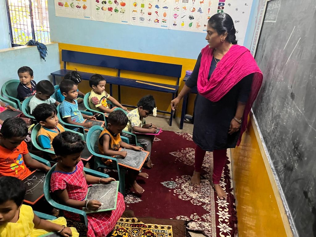 A teacher at the blackboard watching young children write on slates