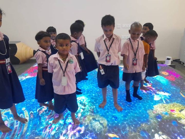 Barefoot children in uniform standing on a glowing, colourful interactive floor projection